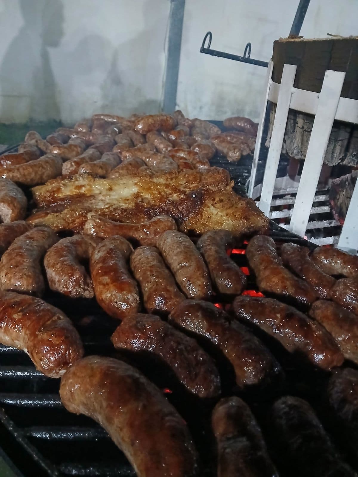 Parrilla llena de chorizos dorados junto a un matambrito, con las brasas encendidas