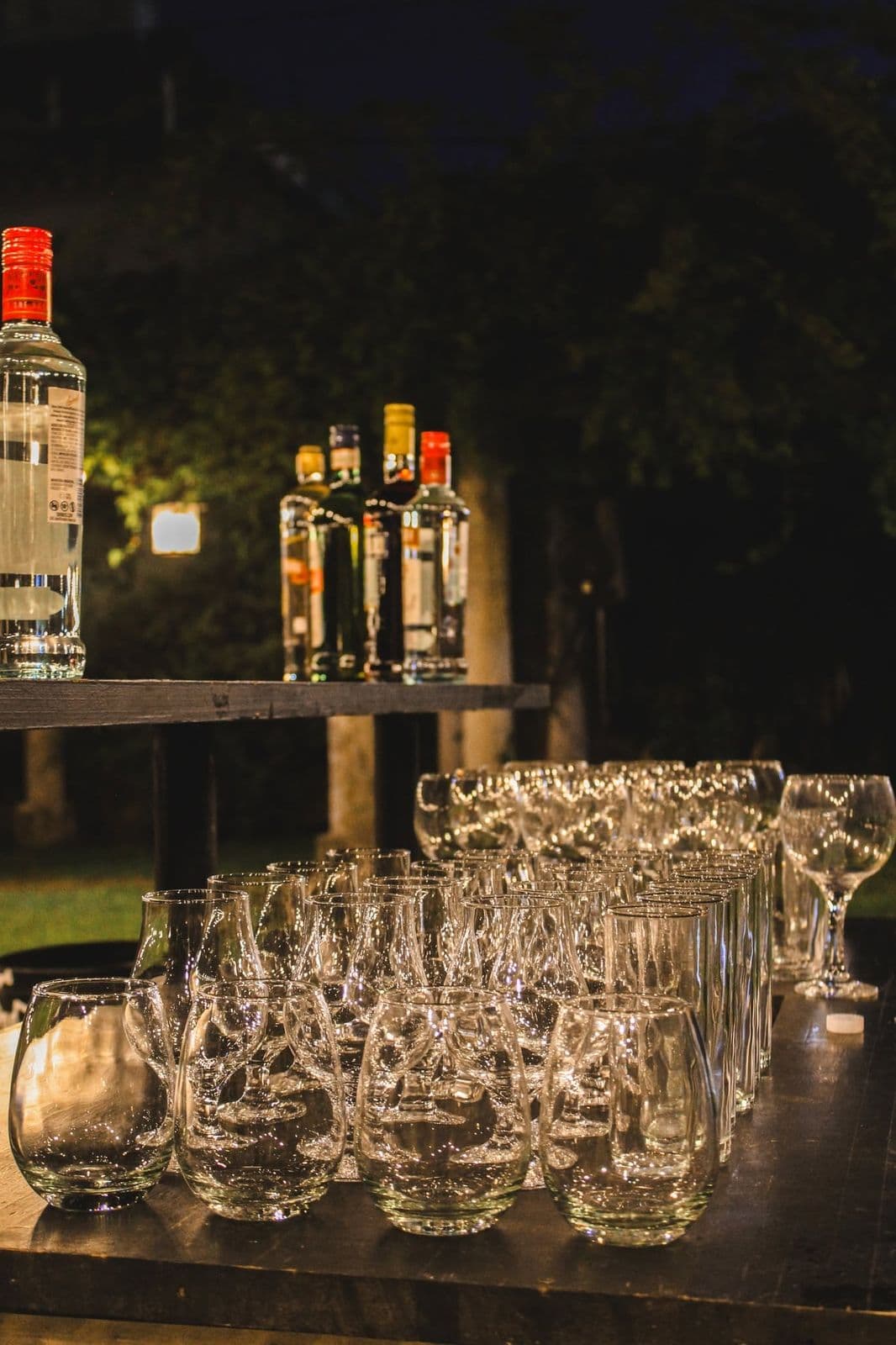 Barra al aire libre de noche, con botellas en un estante y copas y vasos alineados