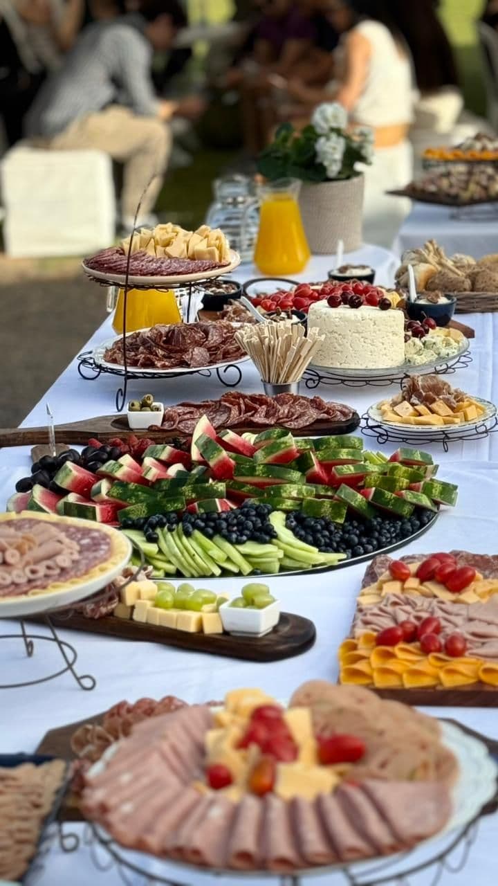 Mesa larga de fríos al aire libre: fiambres, quesos, sandía, uvas y arándanos